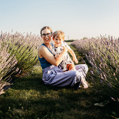 Woman sits between rows of green and purple lavender with small boy in her arms and lap.